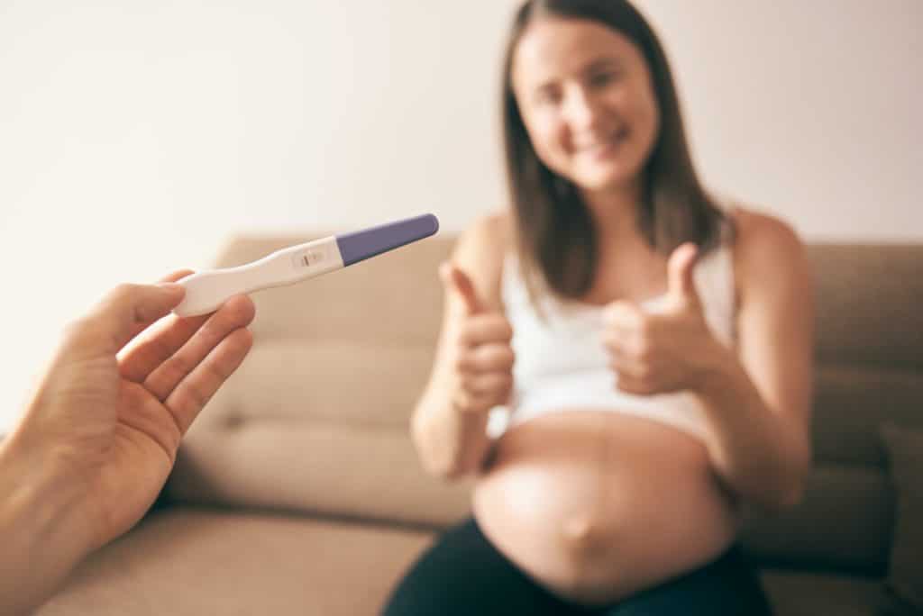 Pregnancy test and happy pregnant woma at backgroung