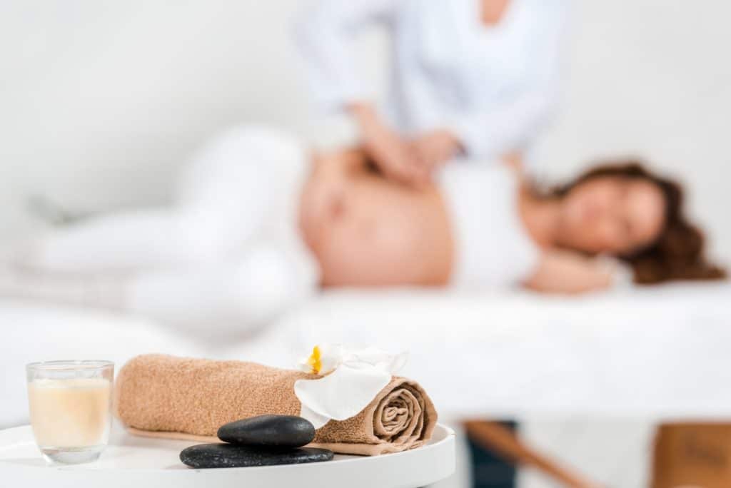 Selective focus of stones, candle with orchid on table and masseur doing massage to pregnant woman